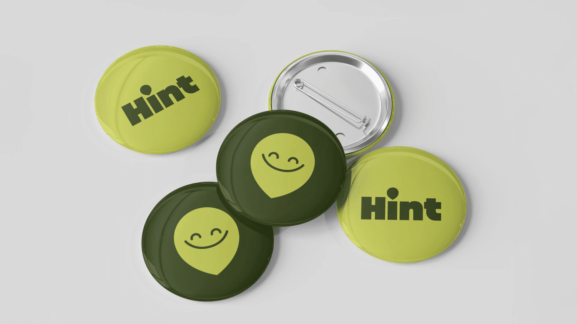 Brand exploration 1.0: lime and olive pin badges with the wordmark and a smiling face