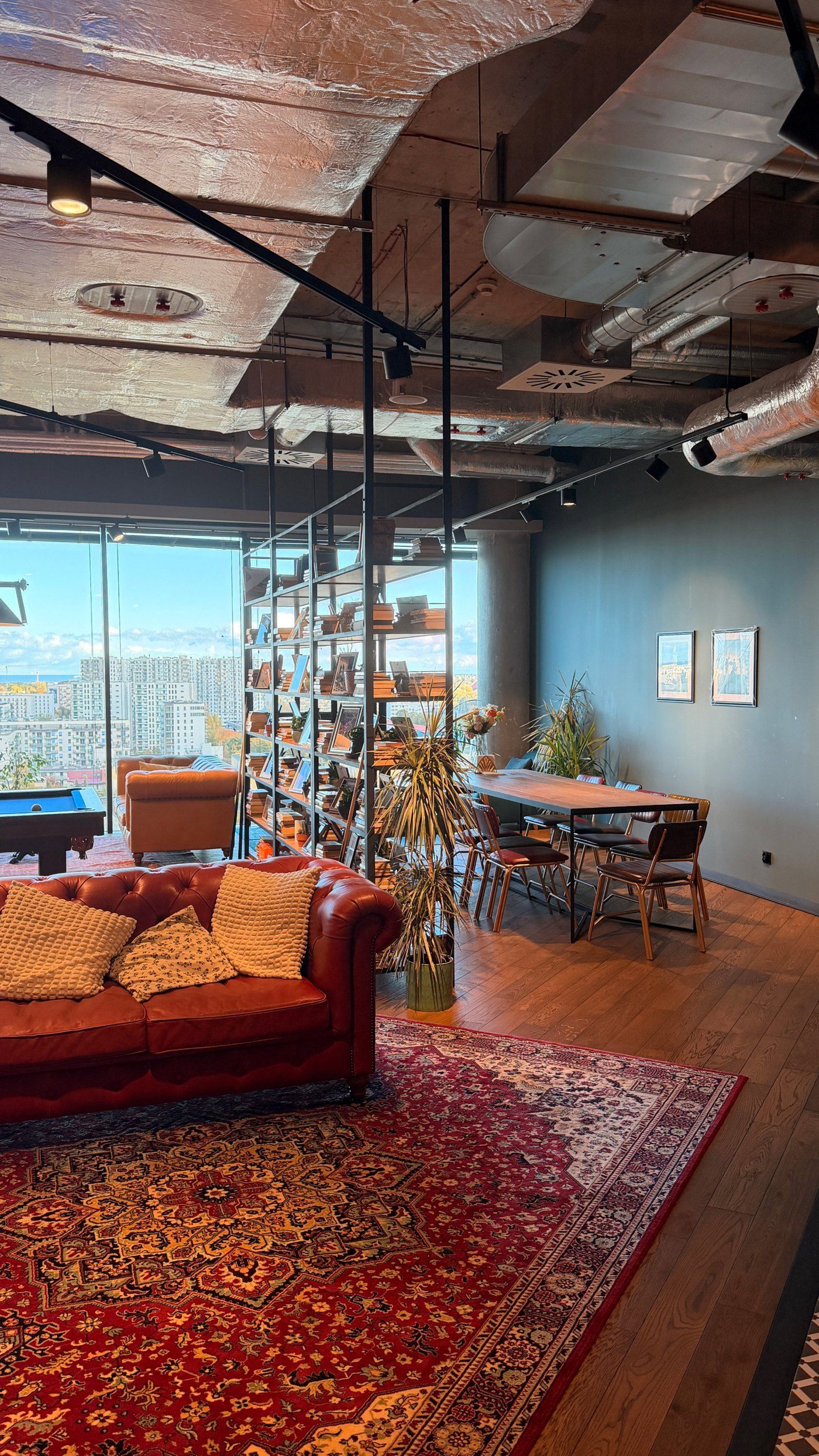 The lounge in the DesignMe office in Gdańsk: a leather sofa, bookshelves, a dining table and floor-to-ceiling windows over the city