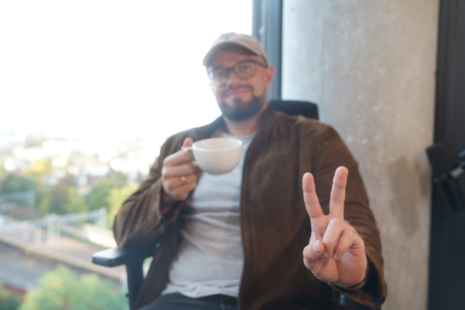 A team member in a cap holding a coffee cup and making a peace sign