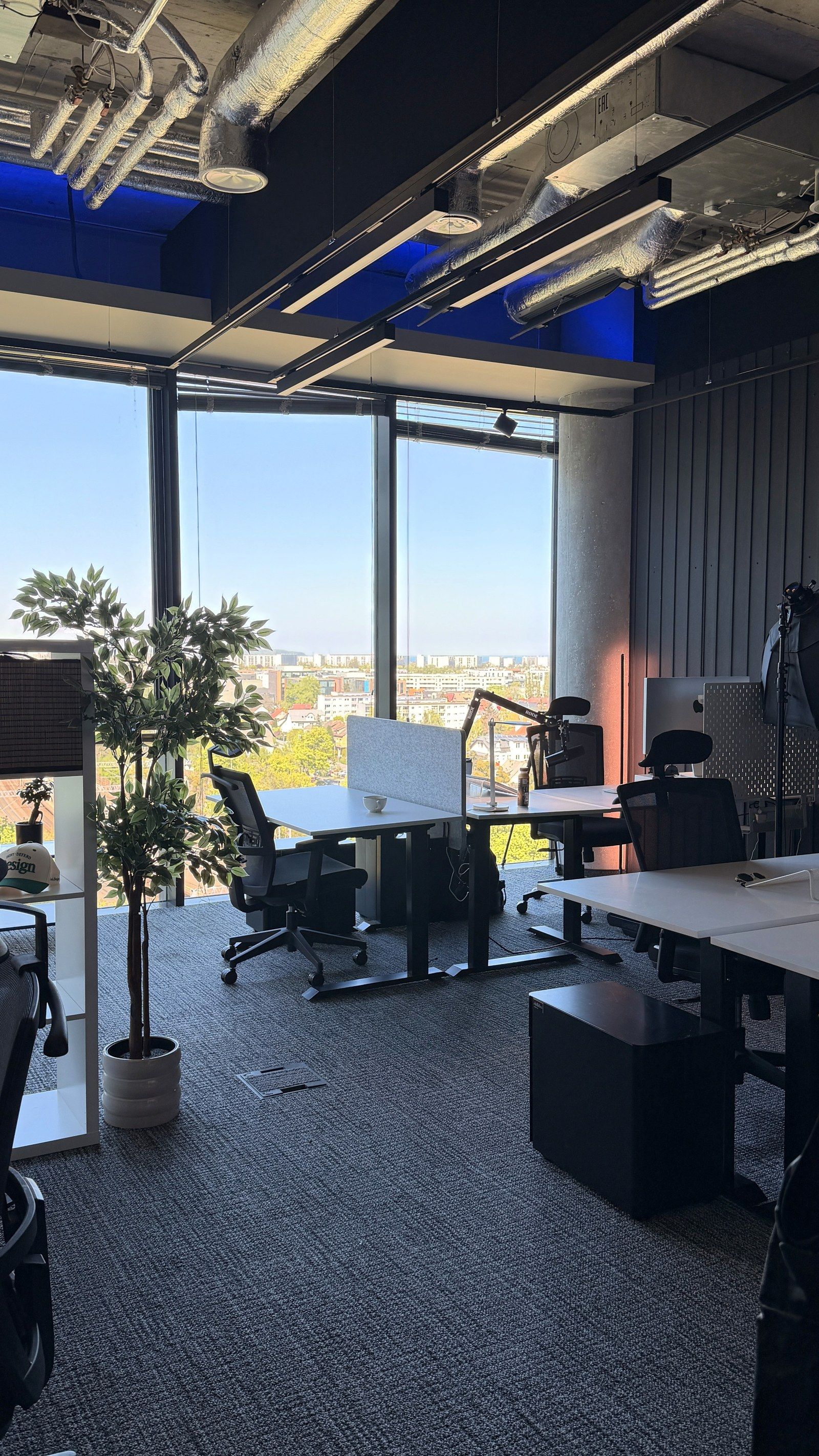Empty desks with monitors by floor-to-ceiling windows in the DesignMe office