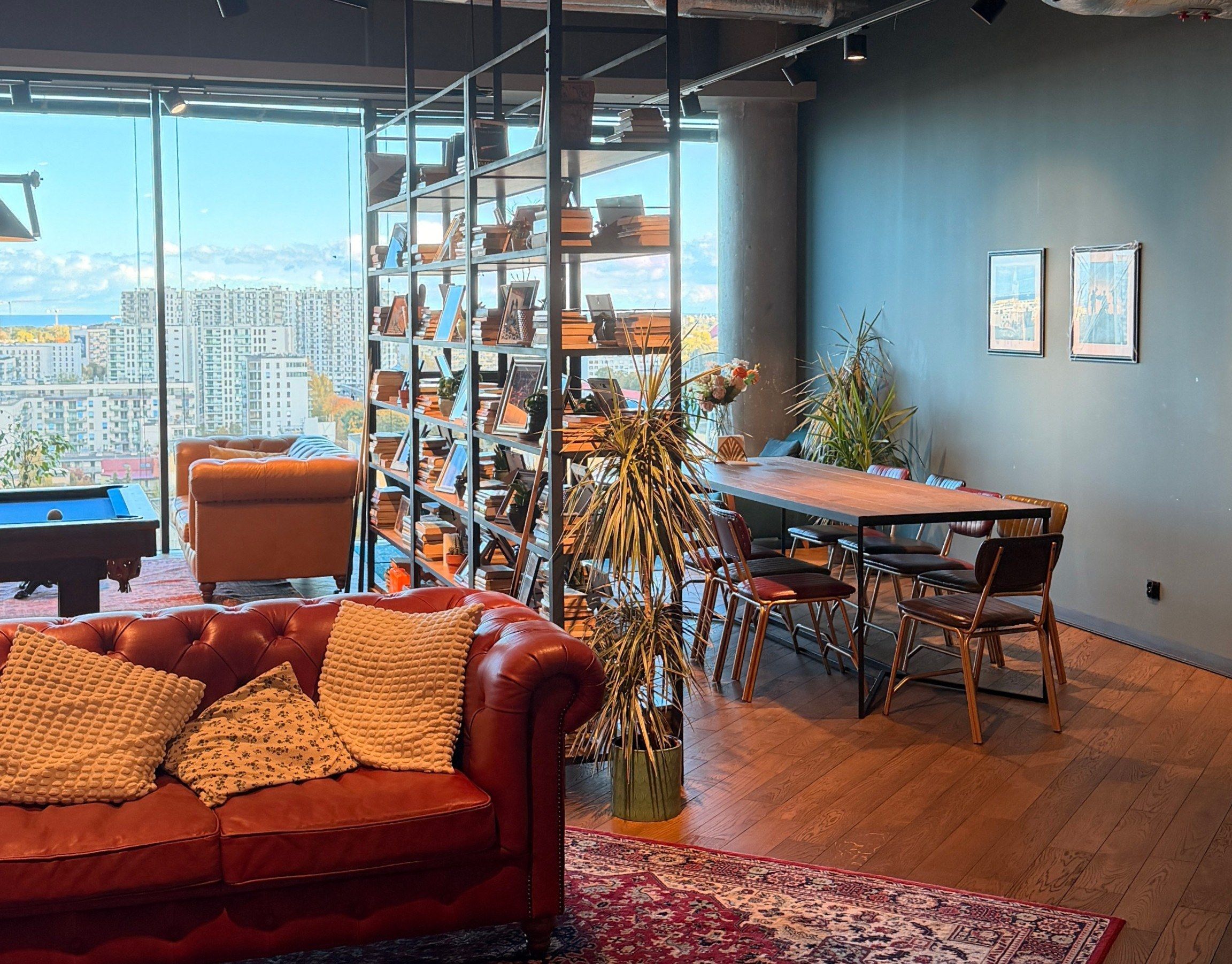 DesignMe office lounge in Gdansk with a leather sofa, pool table, bookshelves and a long dining table by the windows