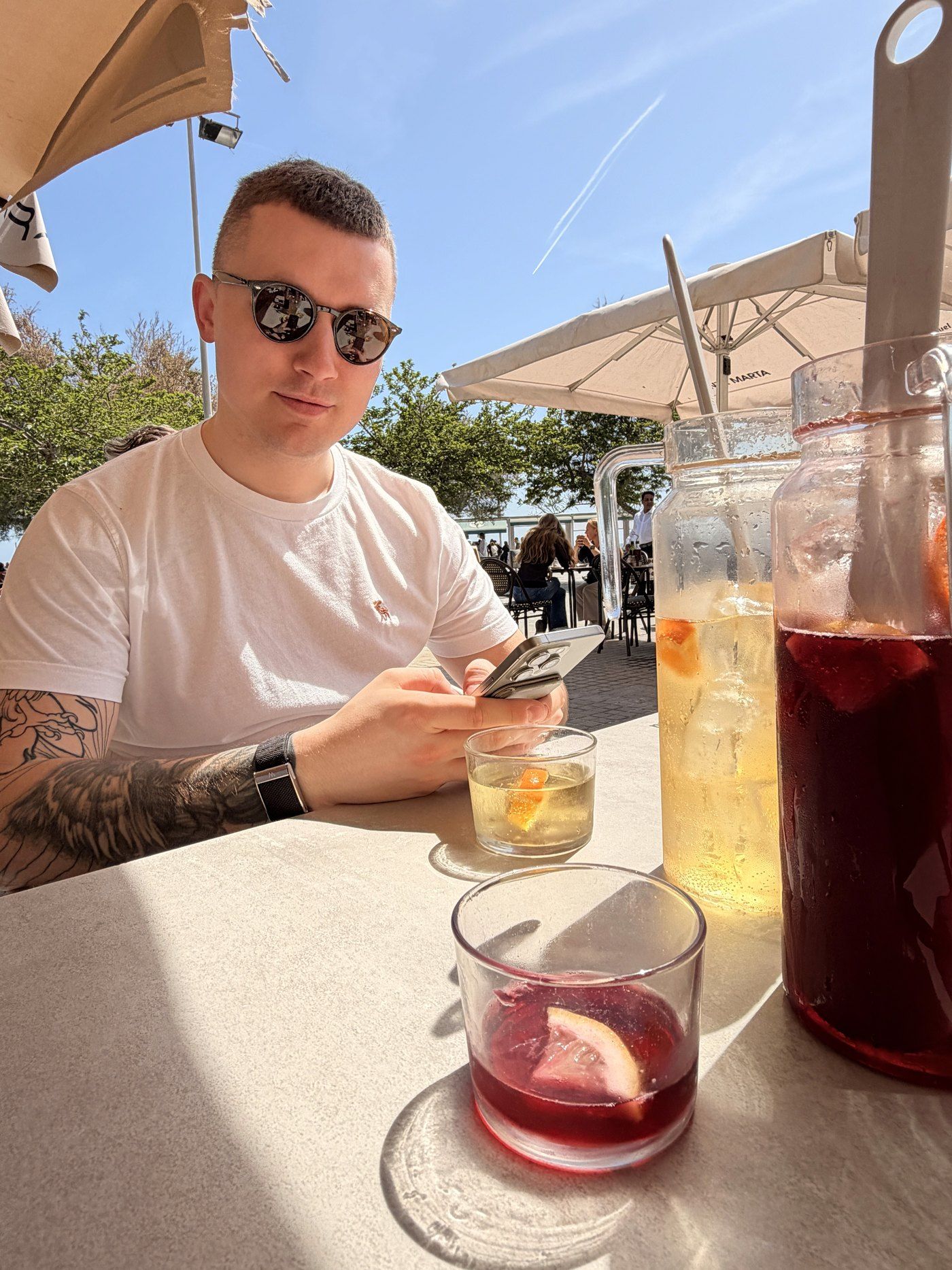A DesignMe team member in sunglasses at a sunny rooftop café table with drinks